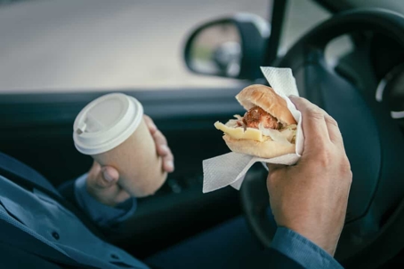 Person eats a sandwich and drinks coffee while driving